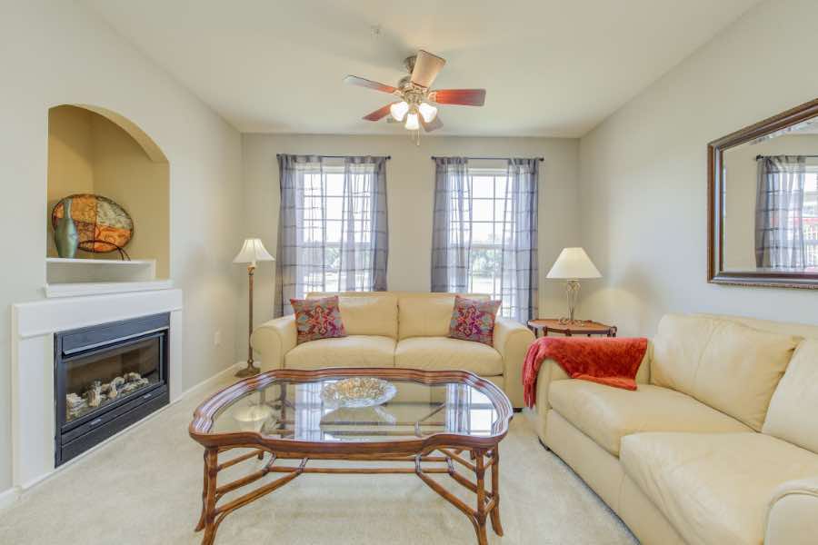 Apartment living room with fireplace, cream-colored furniture, and glass table.